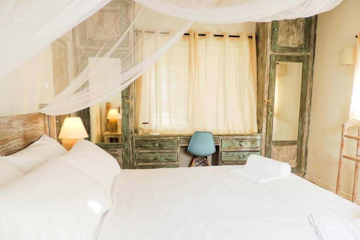 Un dormitorio con cama, una silla, cómoda y espejo.