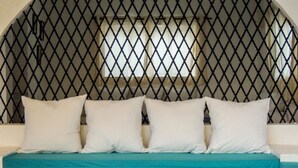 Una cama con colcha color turquesa y cuatro almohadas, cabecero de madera y camino de mesa estampado.