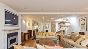 A modern living room with a fireplace, a large sofa, a coffee table, and a spiral staircase leading to an upper level. - The Brendan Gleeson Suite - hiphipstay (Dublin)