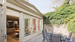 A patio area with a table and chairs, a staircase leading to an upper level, and a stone wall with greenery. - The Brendan Gleeson Suite - hiphipstay (Dublin)