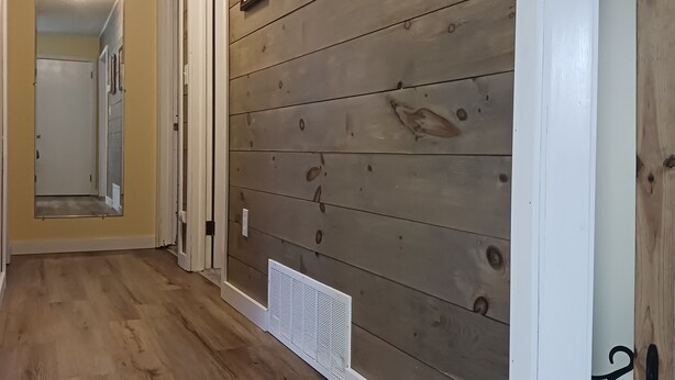 Un pasillo con paneles de madera, un zócalo blanco y una rejilla en el suelo.