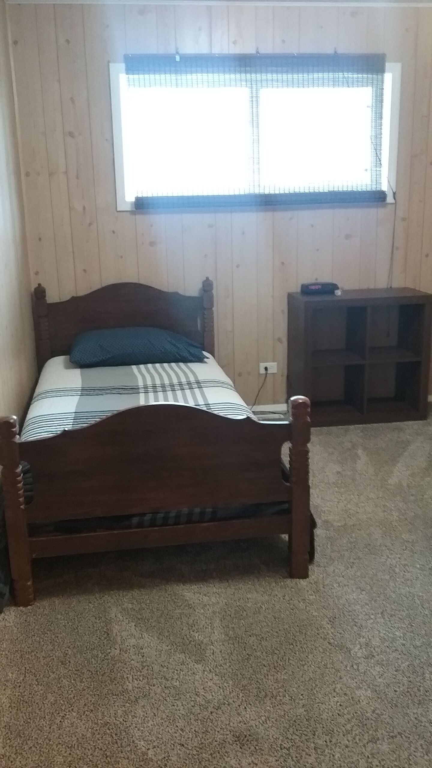 Una cama de madera con colcha de cuadros en una habitación con paredes de madera y una ventana.