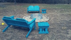 Un área con fogón, banco, una mesa pequeña y una silla Adirondack.