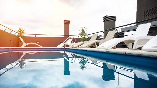 Ein Pool auf dem Dach mit Liegestühlen und Palmen.