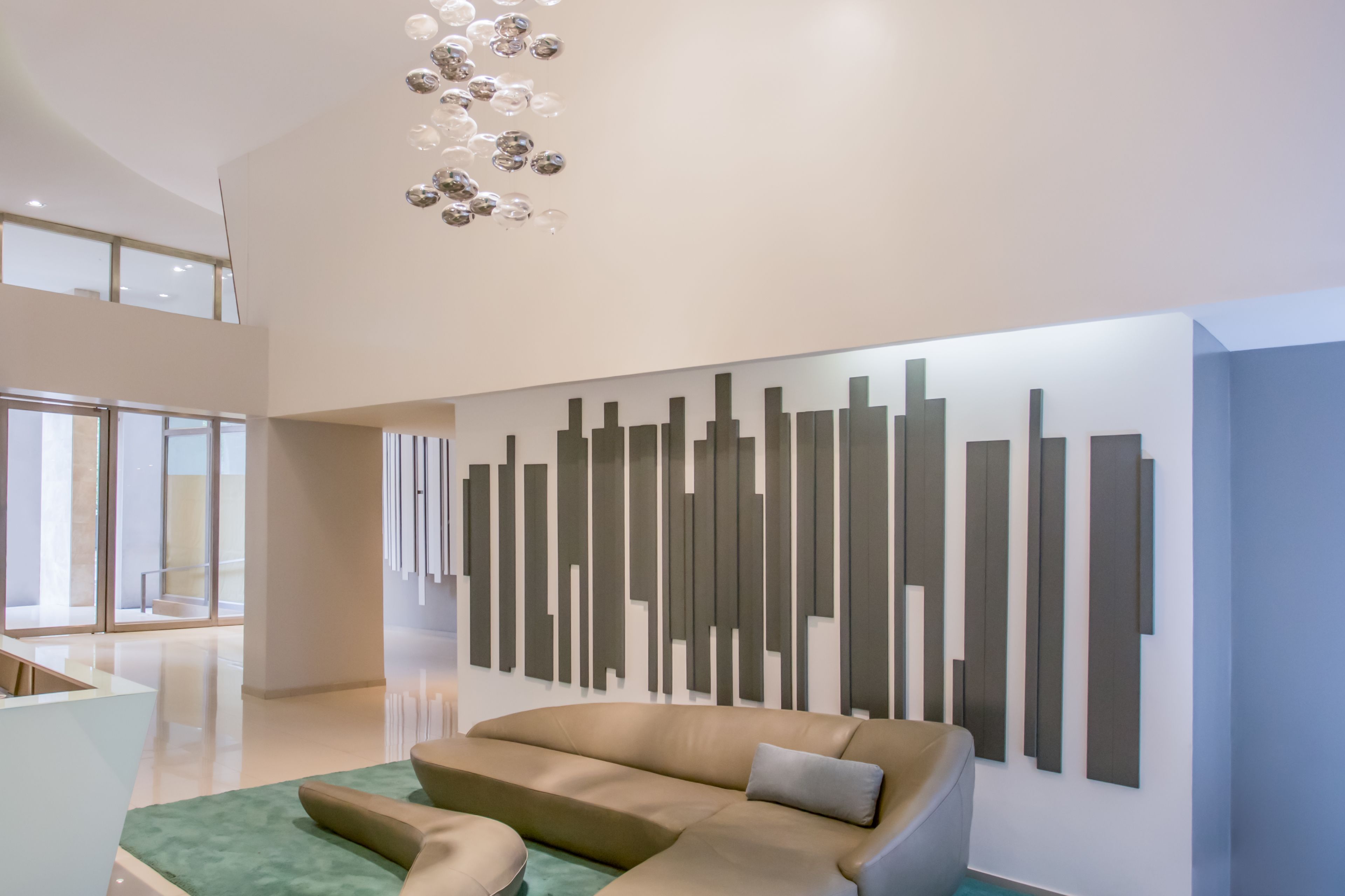 A modern lobby with a high ceiling, a large sectional sofa, and a contemporary wall art installation.