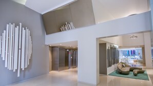 Eine moderne Lobby mit hoher Decke, einem zentralen Aufzug und einer Sitzecke mit grünem Teppich.