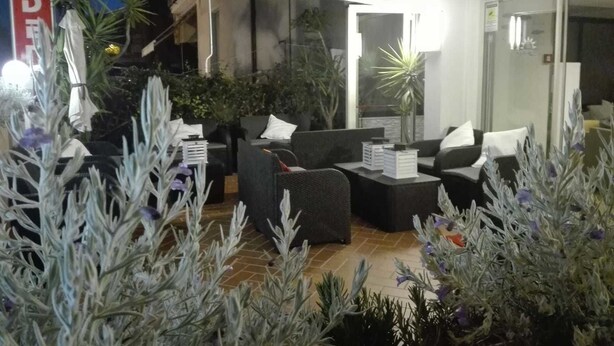 Un espace extérieur aménagé avec des canapés et des tables, entouré de plantes et doté d’un mur en verre.