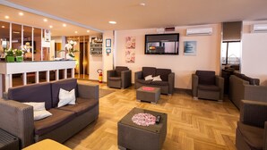 Un hall d’hôtel avec des canapés en osier, un comptoir d’accueil et un téléviseur fixé au mur.