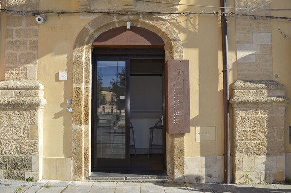 Entrada de un edificio con un arco de piedra, una puerta de cristal y una placa en la pared.