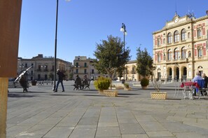 Una plaza pública con bancos, plantas en macetas y un edificio histórico al fondo.