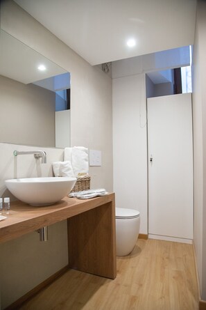Un baño moderno con un lavamanos grande de color blanco, un mueble de tocador de madera, un espejo y un inodoro blanco.