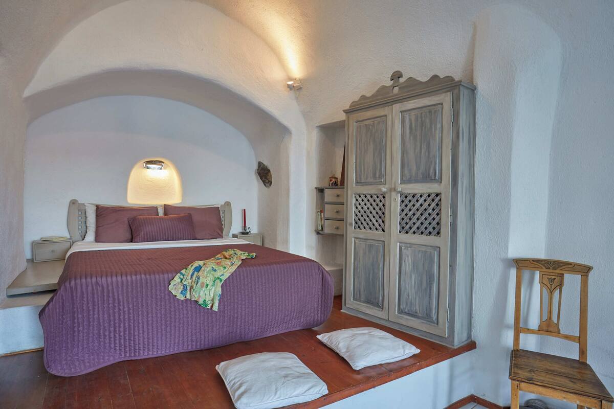 A bedroom with a bed, a nightstand, a wooden wardrobe, and a chair.