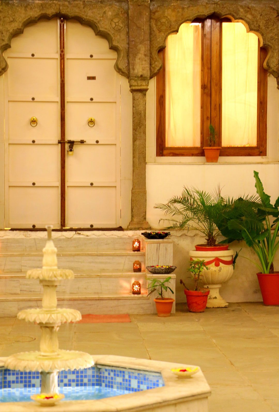 A pool with a fountain, a door with a lock, and potted plants.