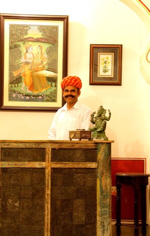 A man standing behind a reception desk with a statue and framed pictures on the wall.