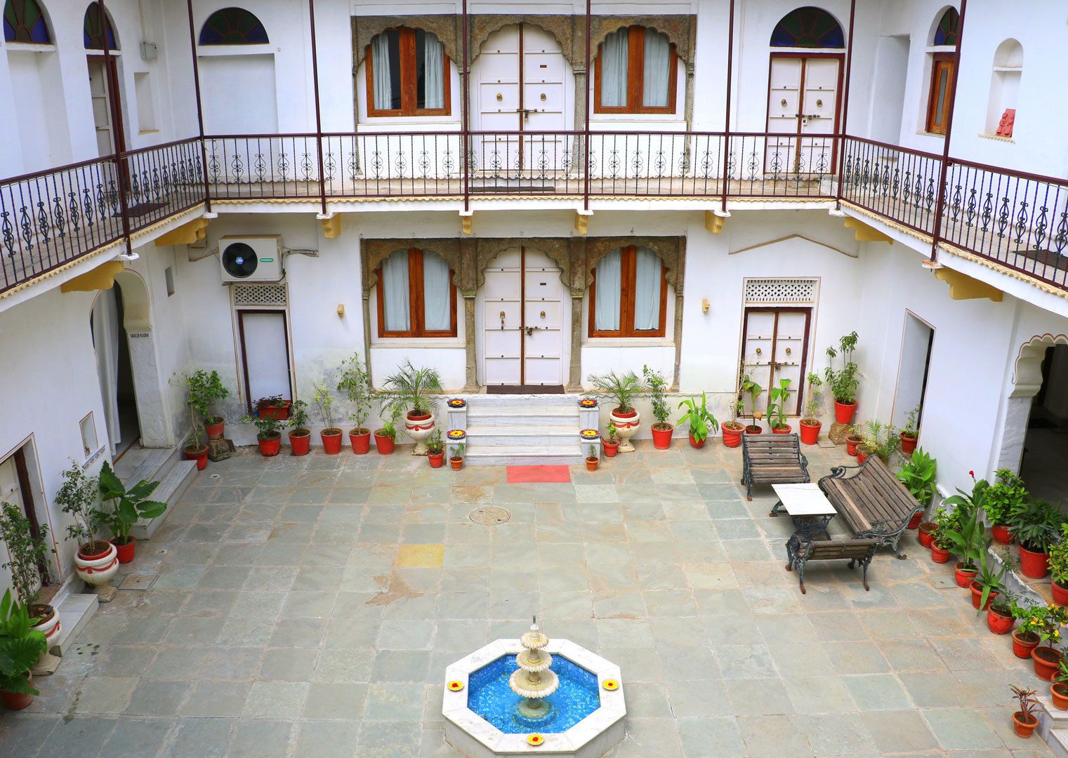 A courtyard with a fountain, potted plants, and a wooden bench.