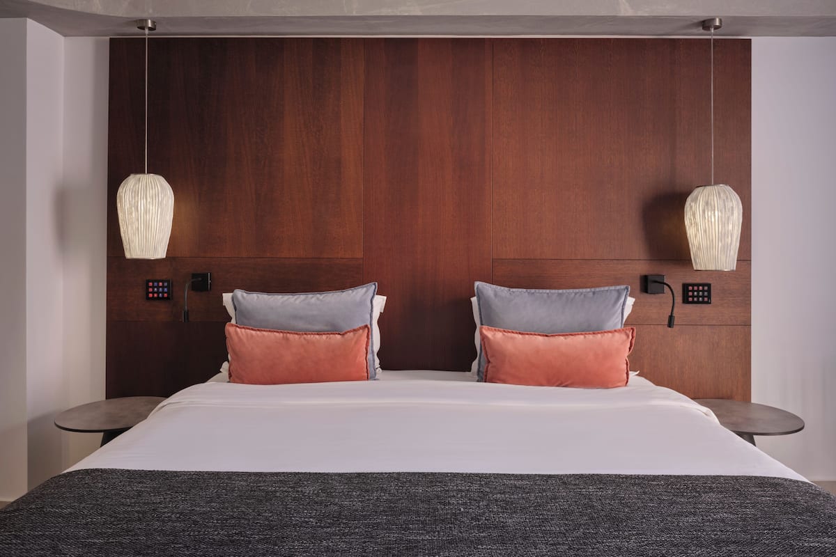 A modern hotel room with a large bed, two bedside tables, a wooden headboard, and pendant lights.