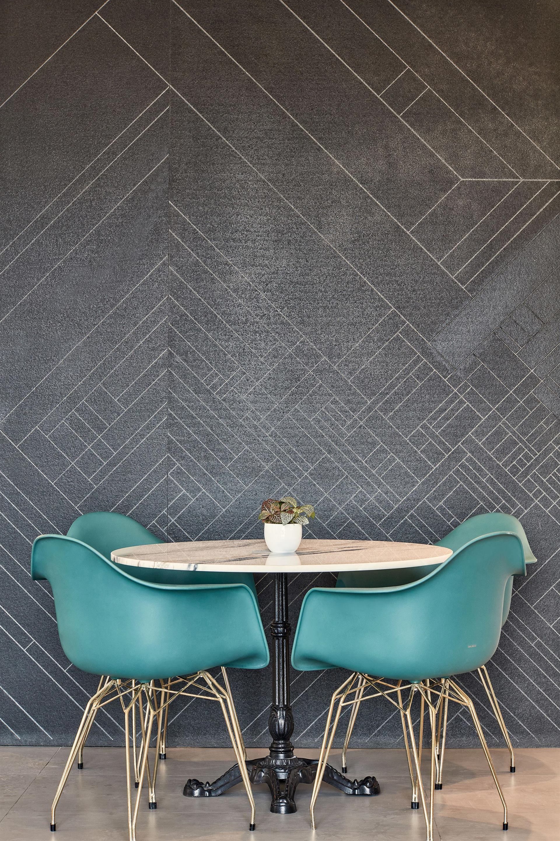 A dining area with a herringbone-patterned wall, a round table, and teal chairs with gold legs.