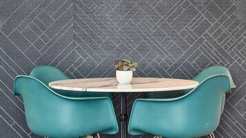 A dining area with a herringbone-patterned wall, a round table, and teal chairs with gold legs.