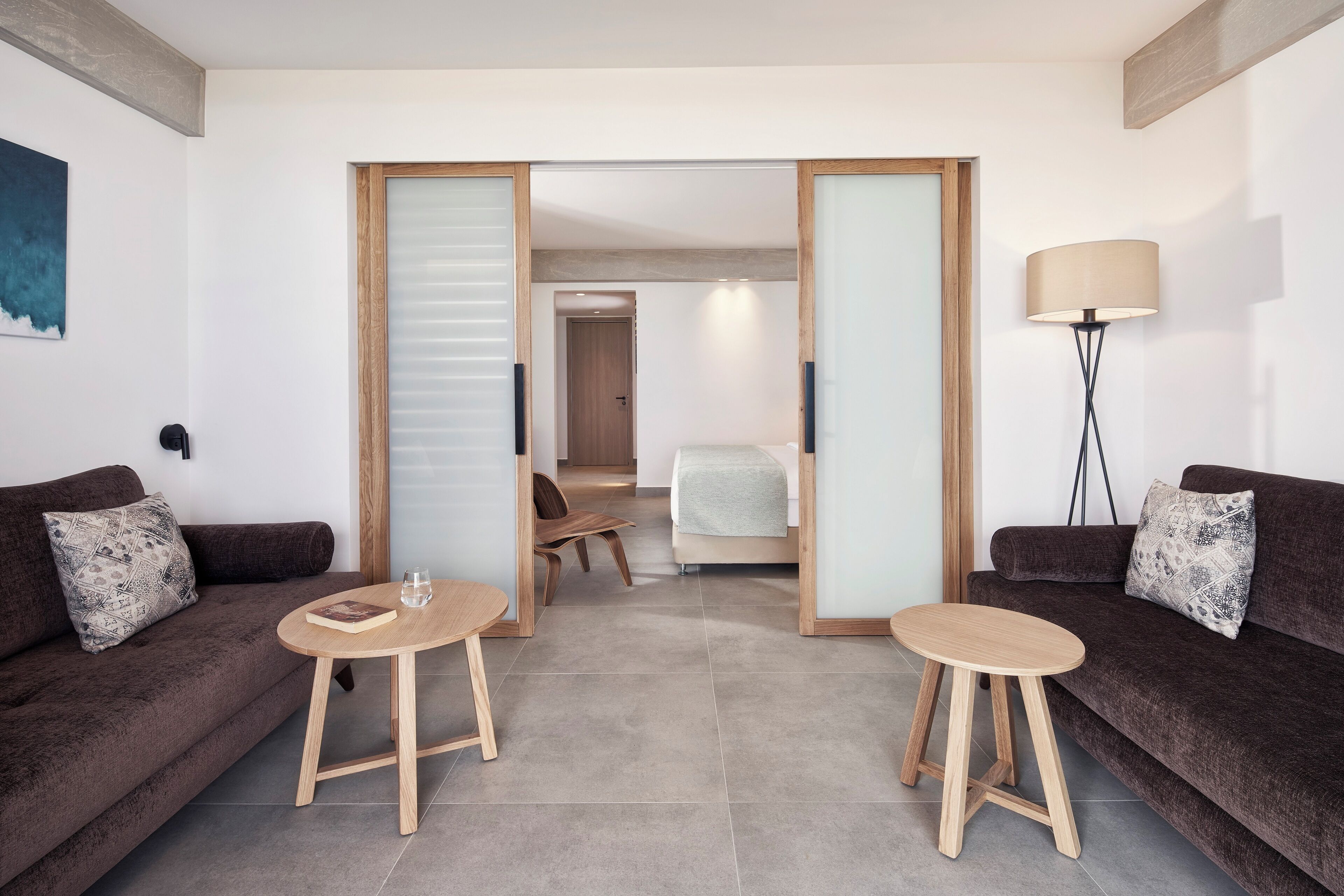 Ein modernes Hotelzimmer mit zwei dunkelbraunen Sofas, einem kleinen Holztisch und einer Stehlampe.