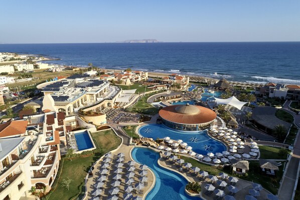 A resort with multiple swimming pools, sun umbrellas, and a large central pool with a dome structure. - Atlantica Caldera Palace - All Inclusive (Hersonissos)
