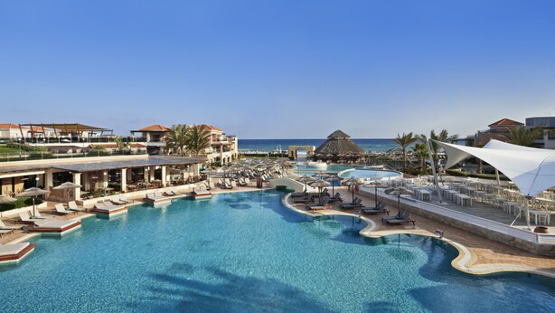 Um resort com uma piscina grande, espreguiçadeiras, guarda-sóis e vista para o oceano.