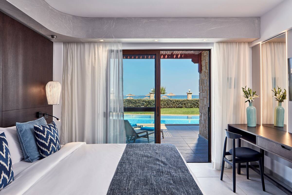 A modern hotel room with a large bed, a desk, and a view of a swimming pool.