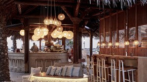 Uma área de bar com disposição circular de assentos, paredes de ripas de madeira, luminárias esféricas pendentes e um balcão com bancos.