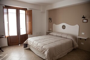 A bedroom with a large bed, a wooden door, a bedside table, and a wall-mounted shelf. - Il Vicoletto B&B (Alfedena)