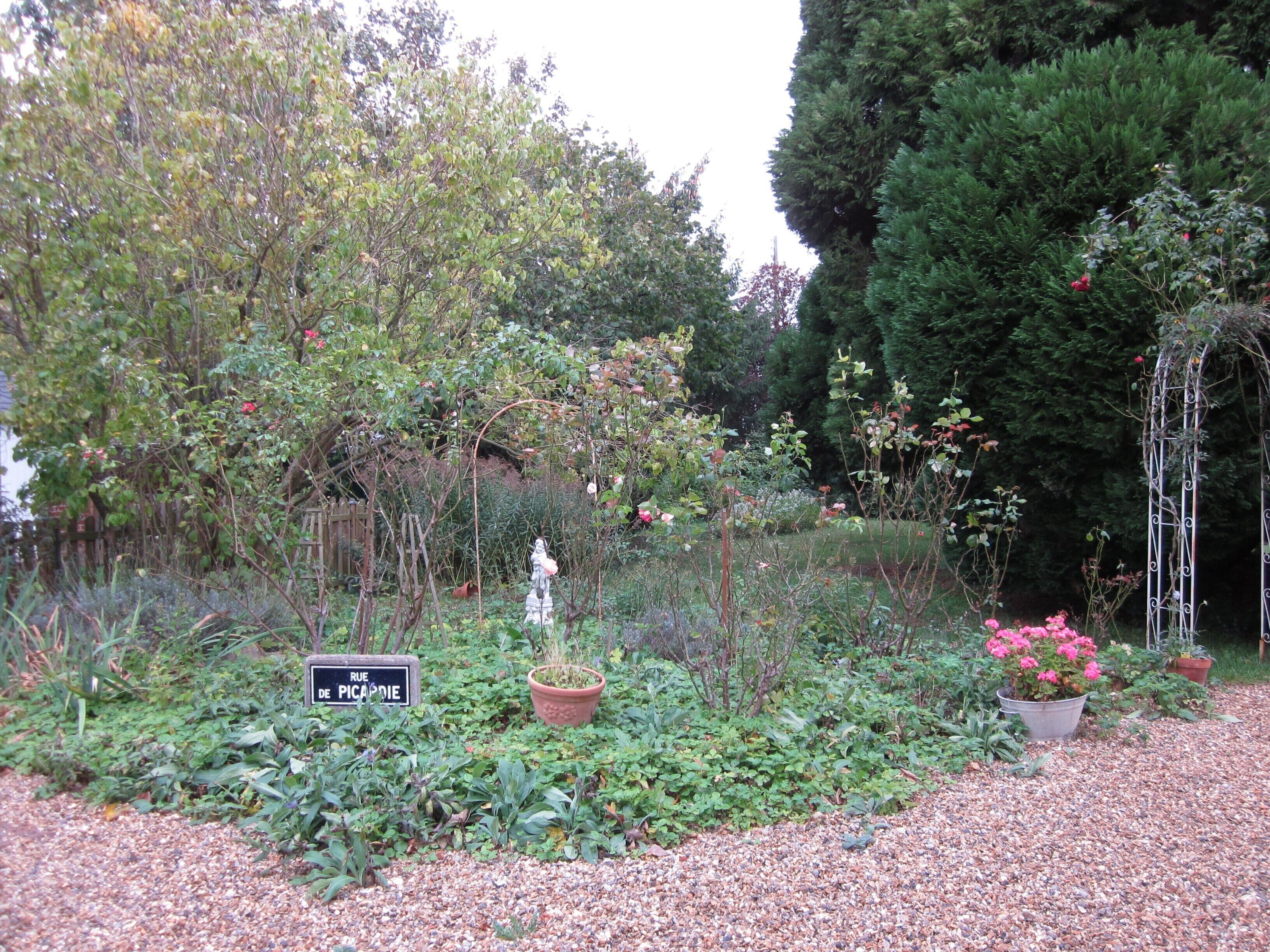 A garden with a variety of plants and a statue. There is a sign that reads "RUE DE PICARDIE".