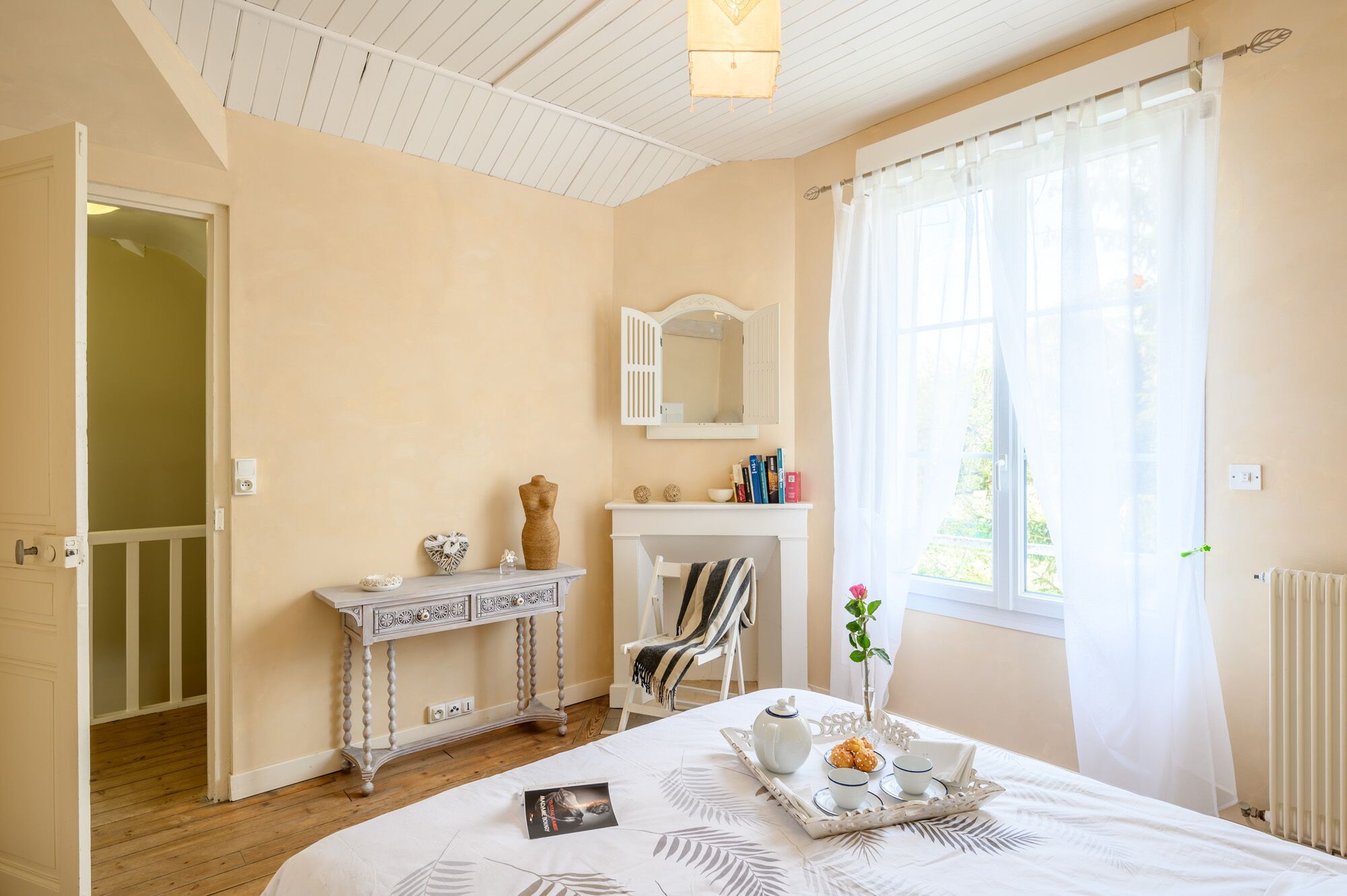 Une chambre à coucher comprenant un lit, une table de chevet, un miroir, une cheminée et une fenêtre avec des rideaux.