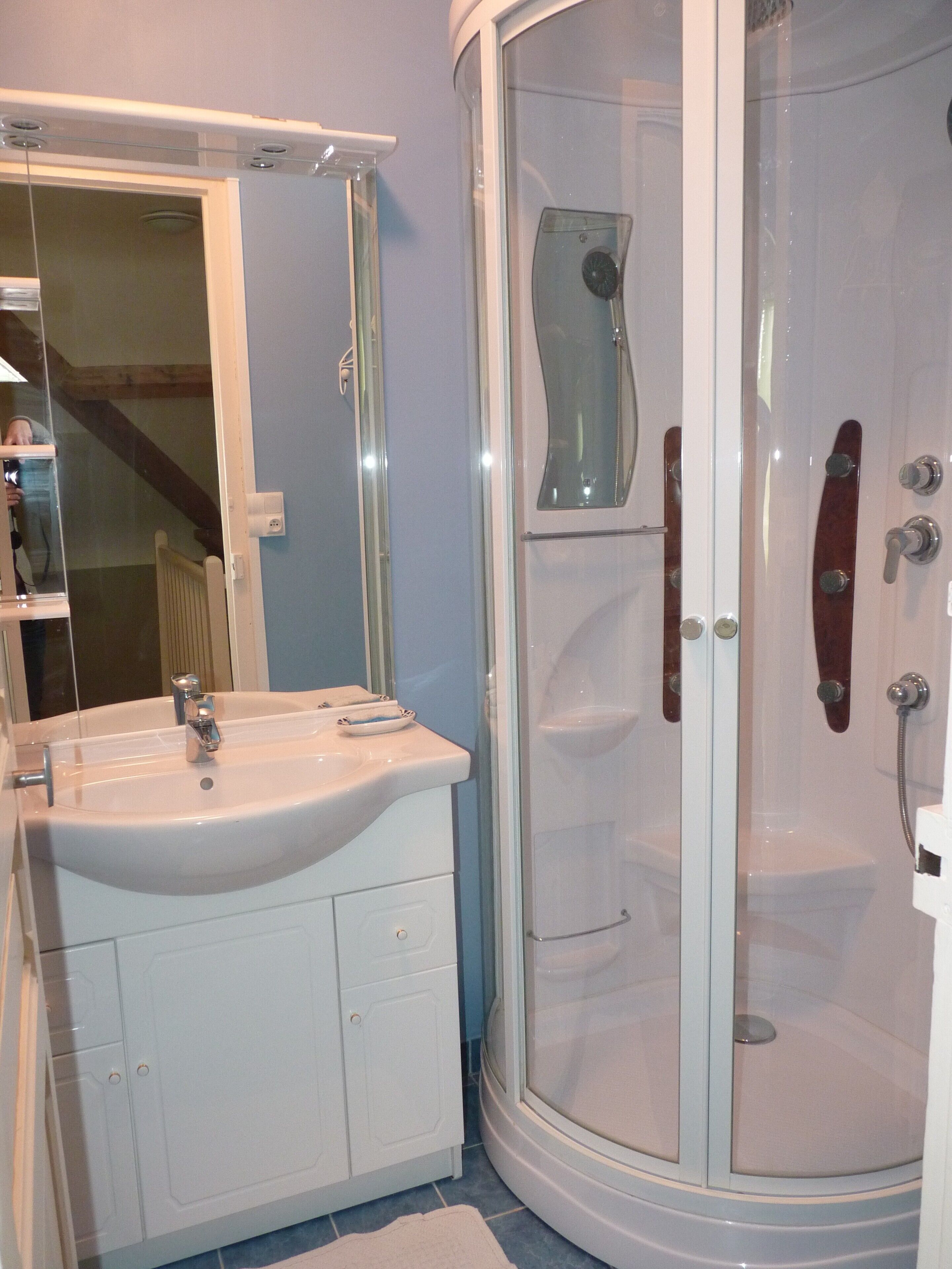 Casa de banho com lavatório branco, espelho e cabine de duche.