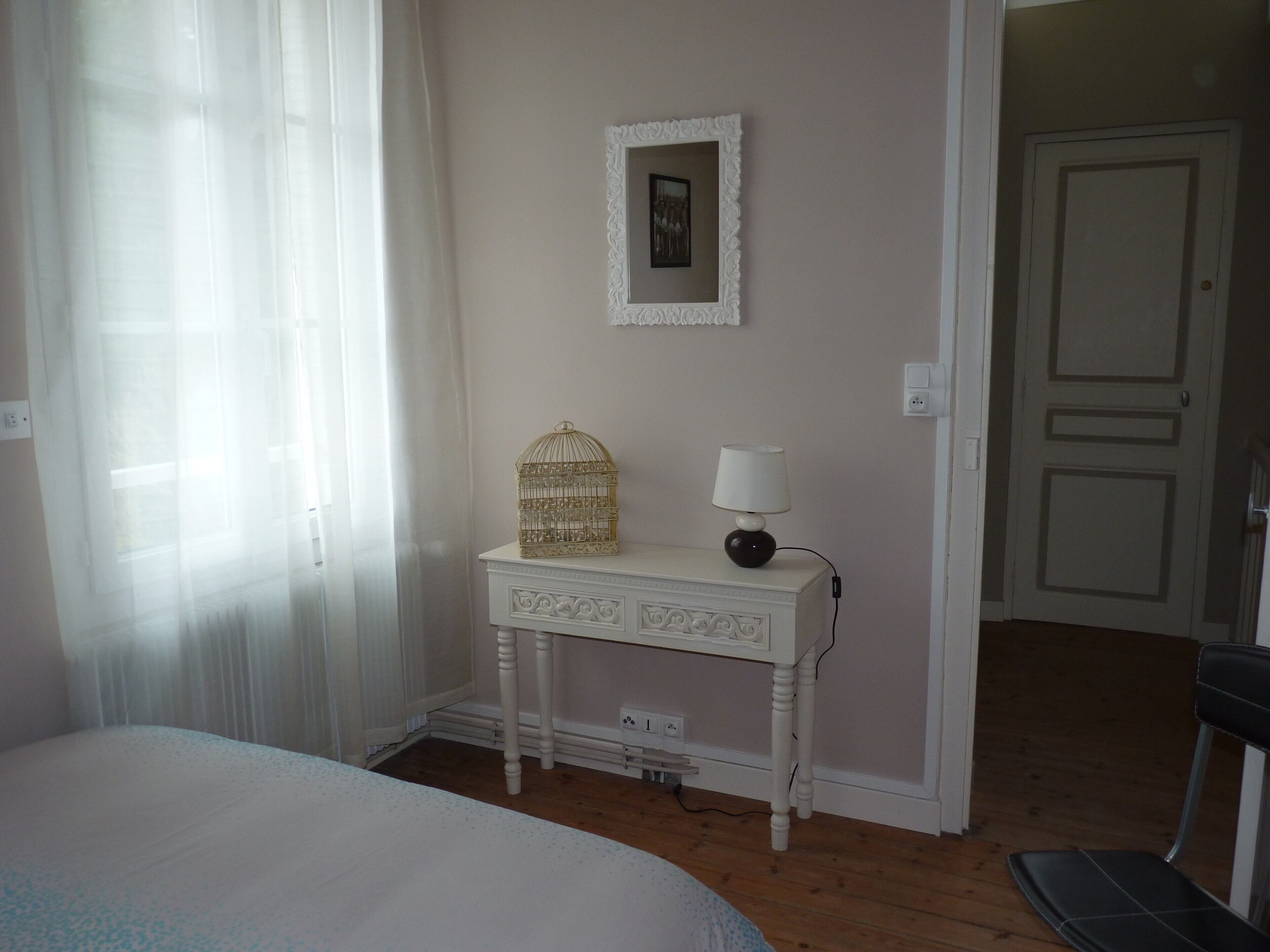 Un dormitorio con cama, una mesita de noche con lámpara, un pequeño adorno y una puerta que da a otra habitación.