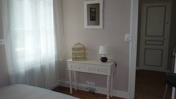 Un dormitorio con cama, una mesita de noche con lámpara, un pequeño adorno y una puerta que da a otra habitación.