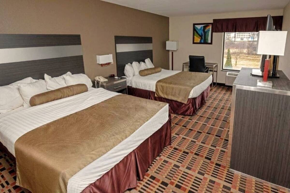 A hotel room with two beds, a desk, a chair, a lamp, and a window with a view.