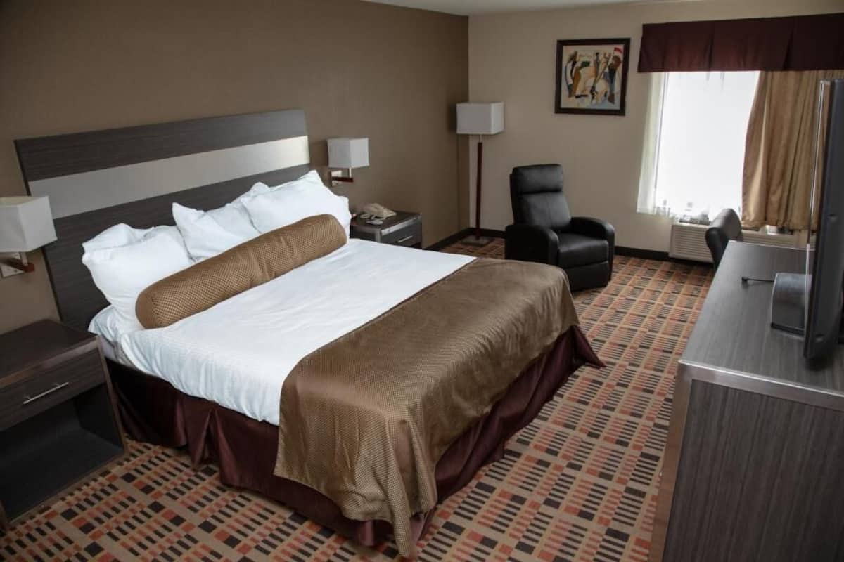 A hotel room with a large bed, a desk with a computer, a chair, and a lamp.