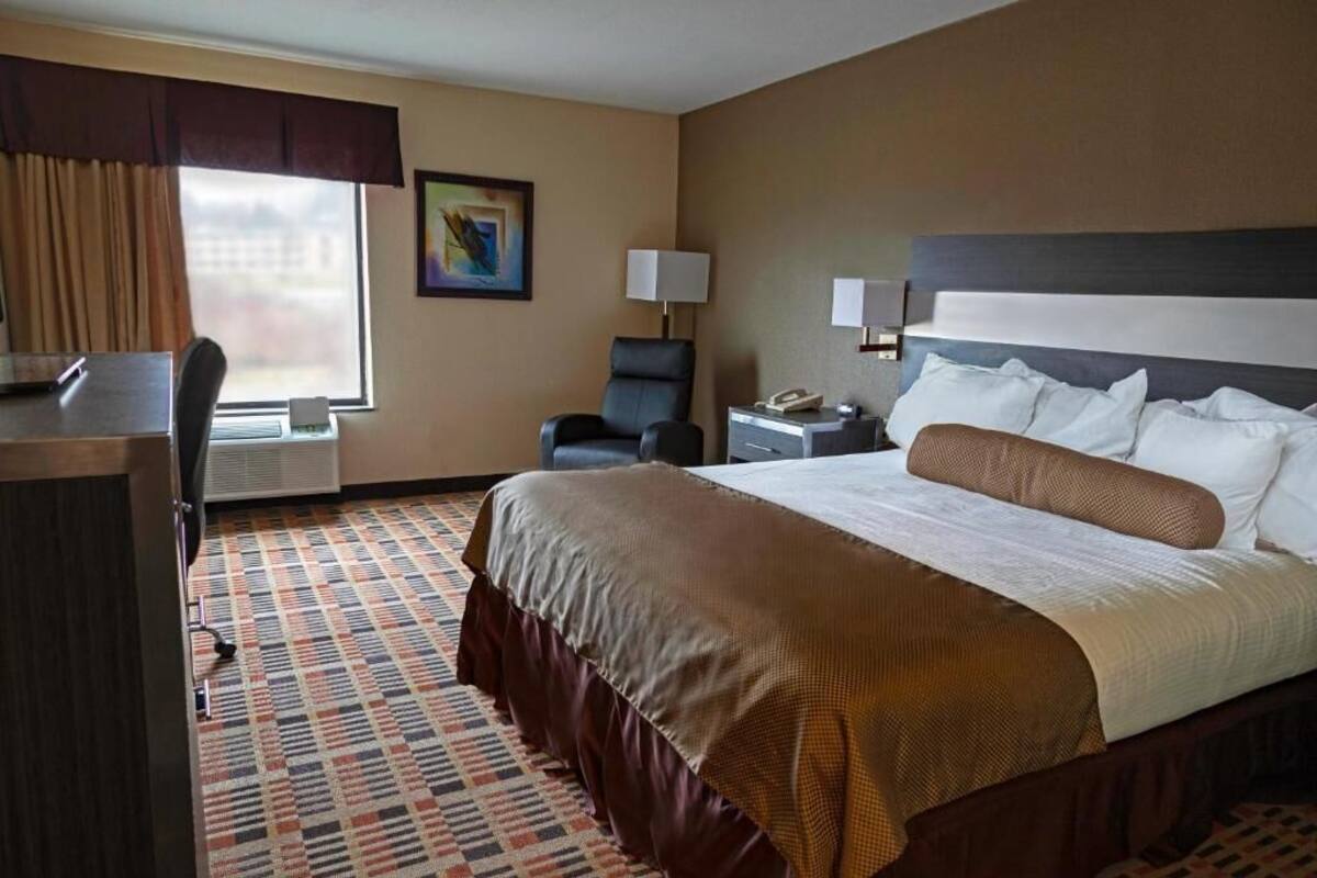 A hotel room with a large bed, a desk, a chair, a desk lamp, and a window with curtains.