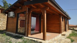 A small wooden cabin with a covered porch, stone foundation, and a large sliding glass door. - Agriturismo Pinelli (Plataci)