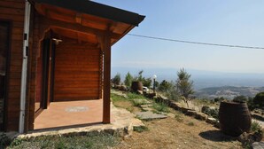 A wooden cabin with a covered porch, a stone pathway, and a view of the landscape. - Agriturismo Pinelli (Plataci)