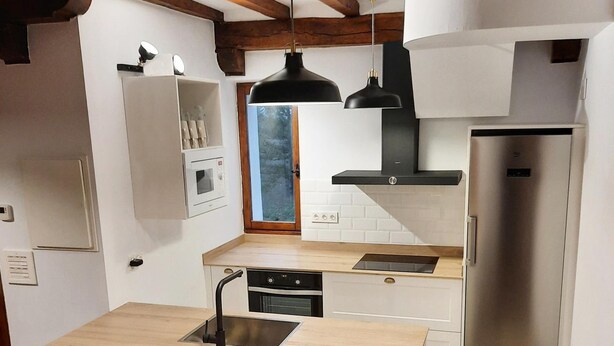 Una cocina moderna con una isla central, electrodomésticos de acero inoxidable y taburetes negros.