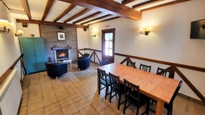 Un interior r ústico con techo de madera, chimenea, una mesa de comedor con sillas y pared de piedra.
