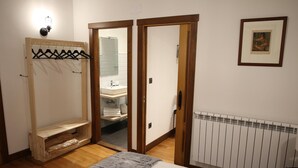 Un dormitorio con cama, un armario de madera, un baño visible a través de una puerta abierta y un radiador.