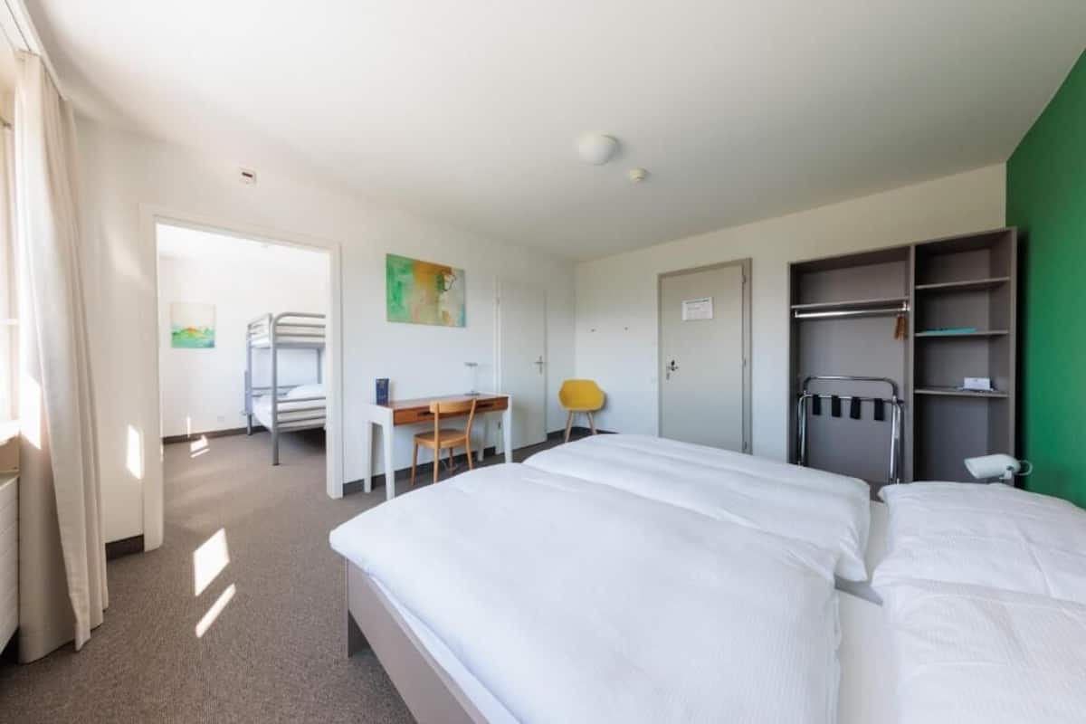 A hotel room with two beds, a desk, a chair, a wardrobe, and a bathroom door.