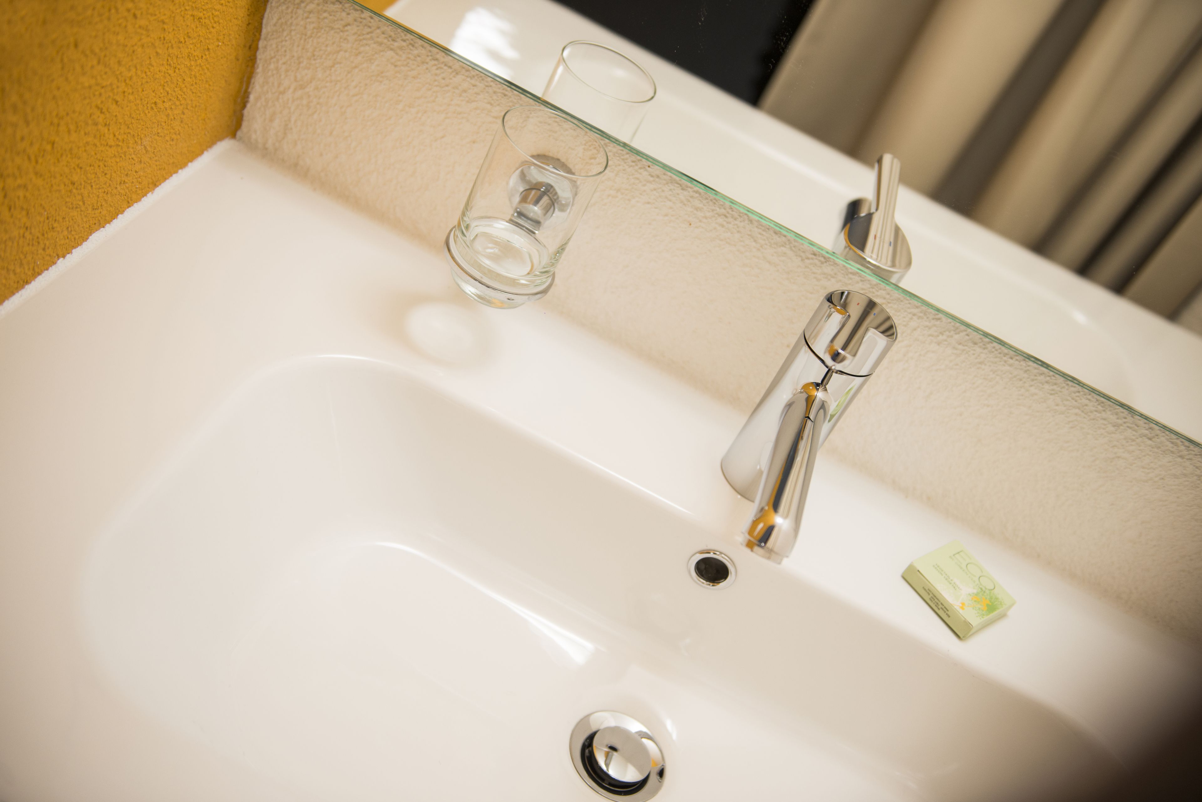 A white bathroom sink with a glass partition, a chrome faucet, and a soap dish.