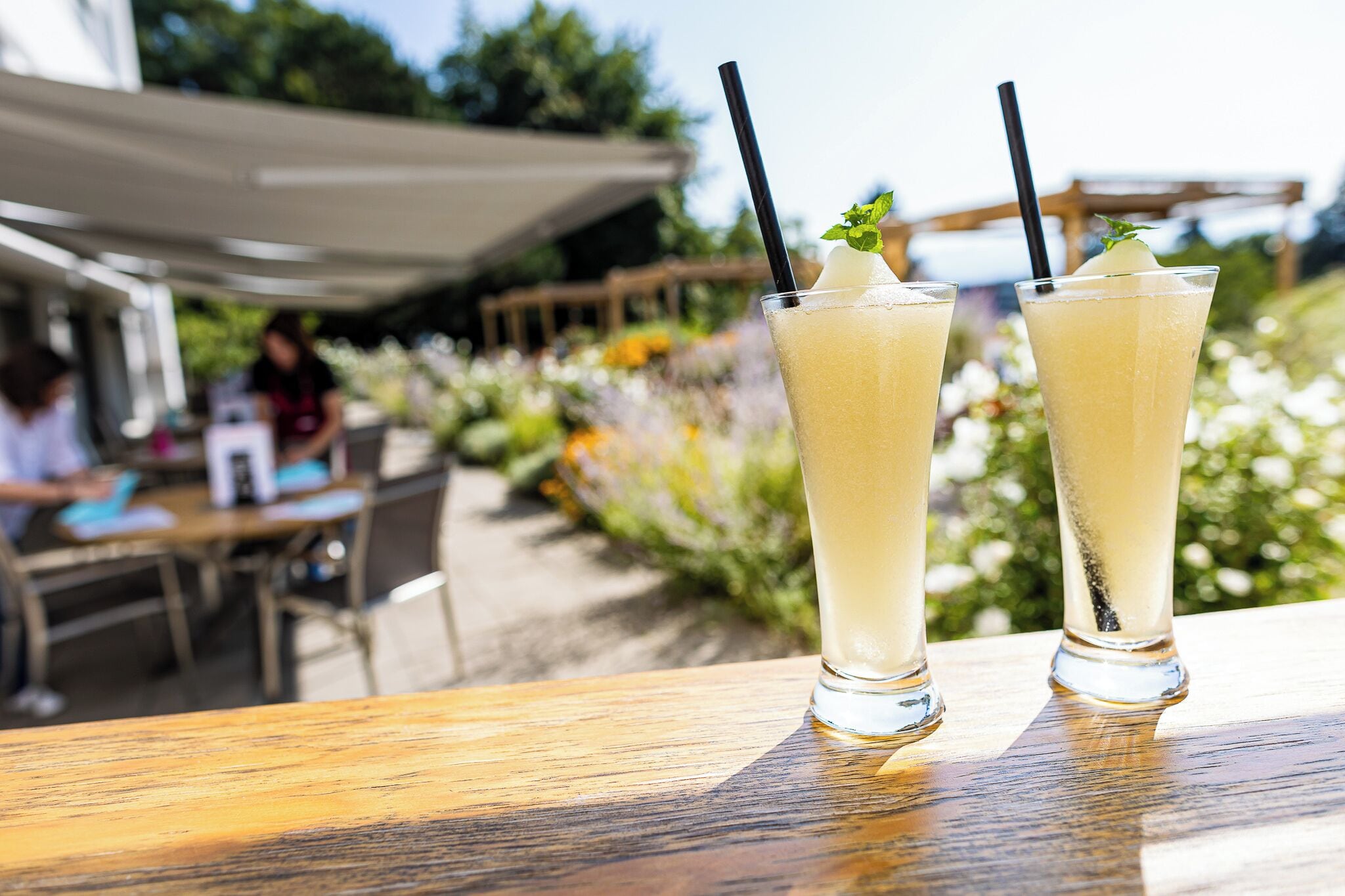 Deux grands verres contenant une boisson claire, accompagnés de pailles et décorés de feuilles de menthe, sont posés sur une table en bois.