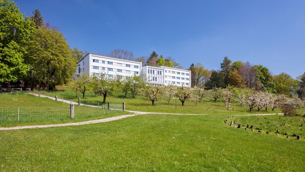 A grassy field with a white building in the background. - Domaine NDR (Villars-sur-Glane)