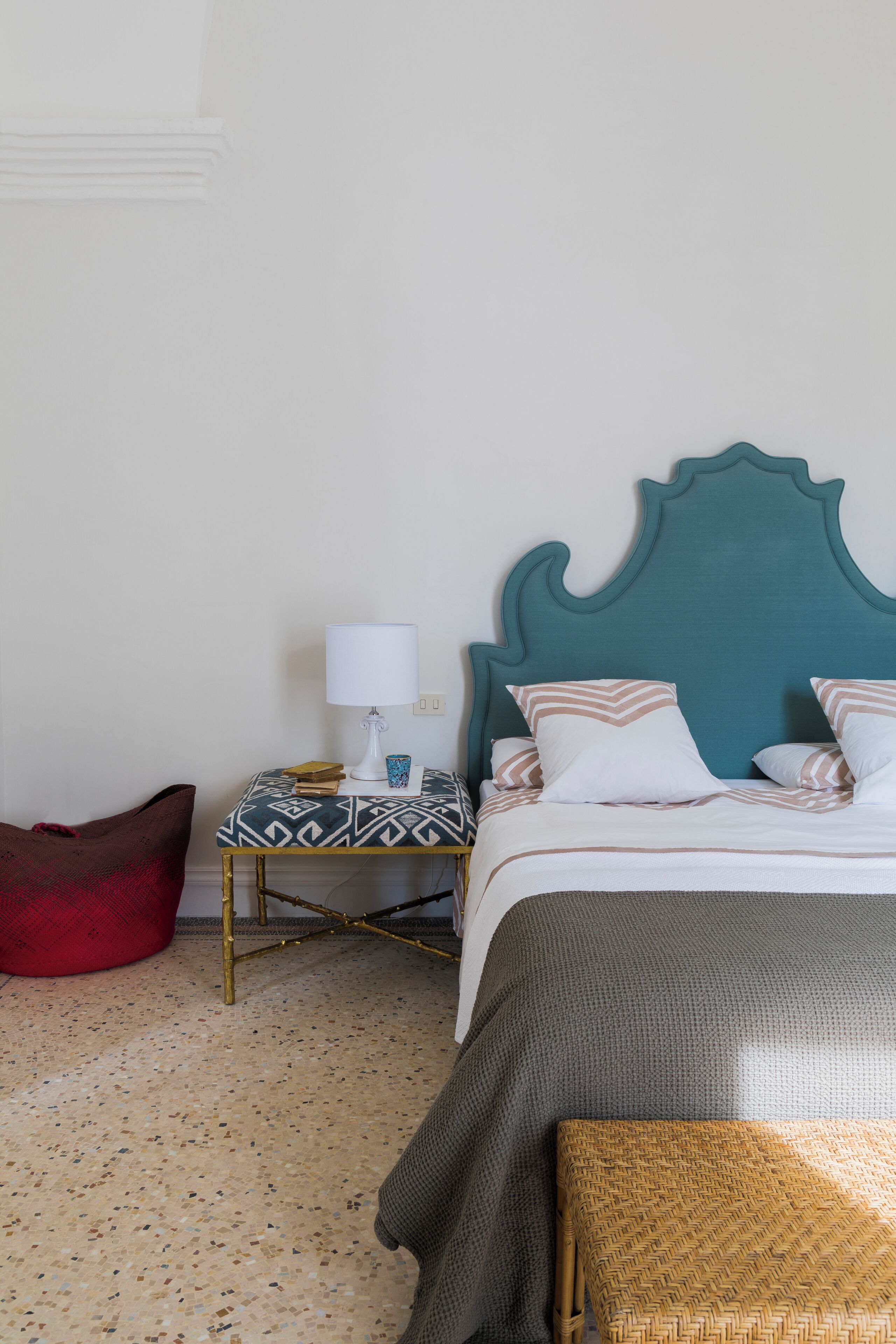 Un dormitorio ordenado con cama, mesita de noche, lámpara y un sillón de peluche rojo.
