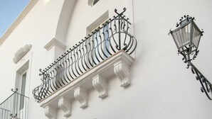 A white building with a wooden door, a balcony with wrought iron railings, and a street lamp. - Palazzo Maritati (Nardò)