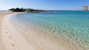 A clear beach with footprints, a sandy shore, and a tower structure in the background. - Palazzo Maritati (Nardò)