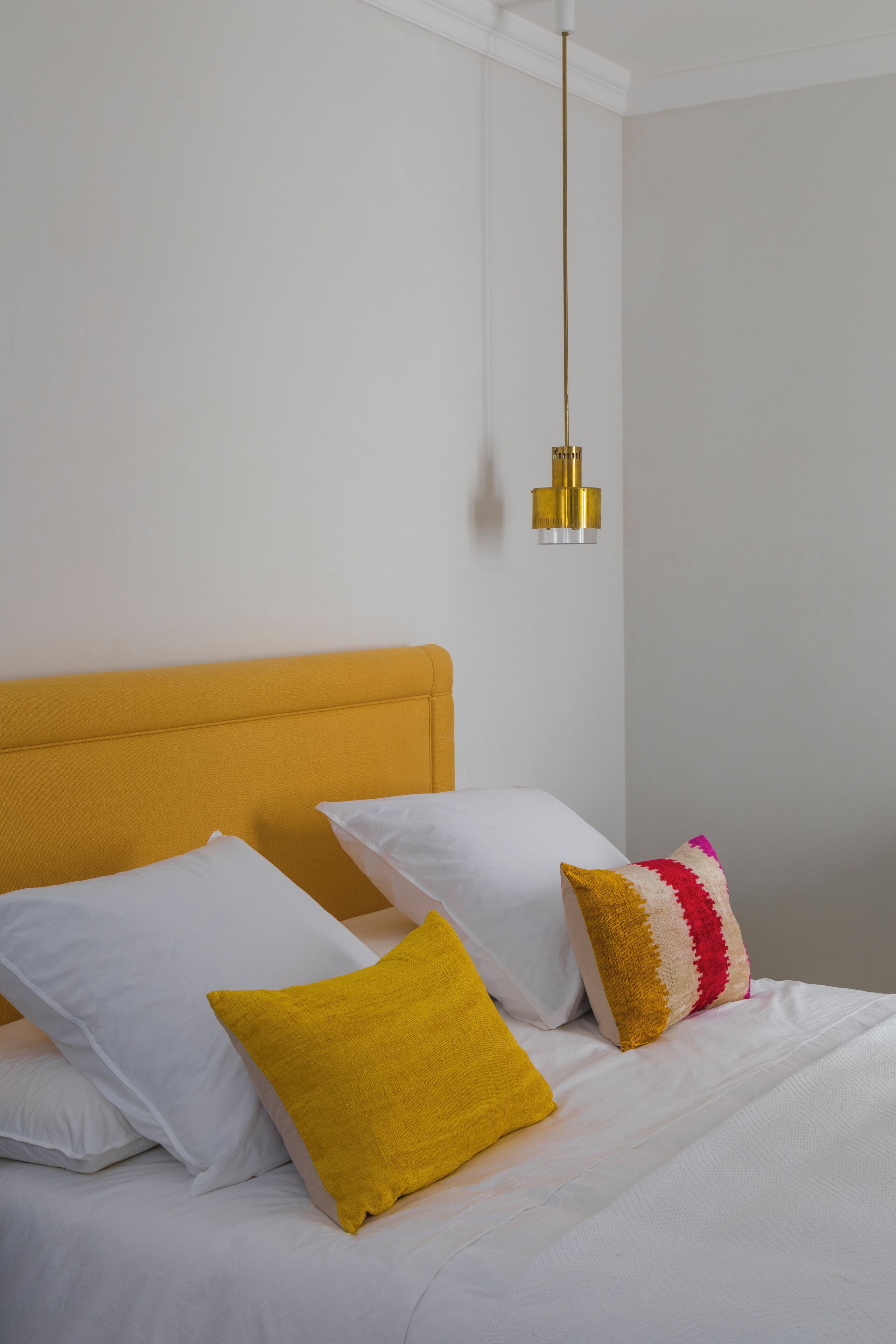A bed with white bedding and a mustard-colored headboard.