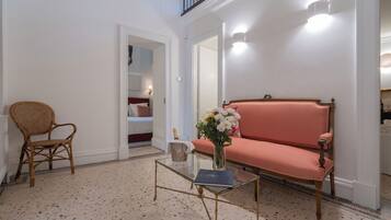 A room with a red upholstered sofa, a wicker chair, a glass coffee table, and a vase with flowers.
